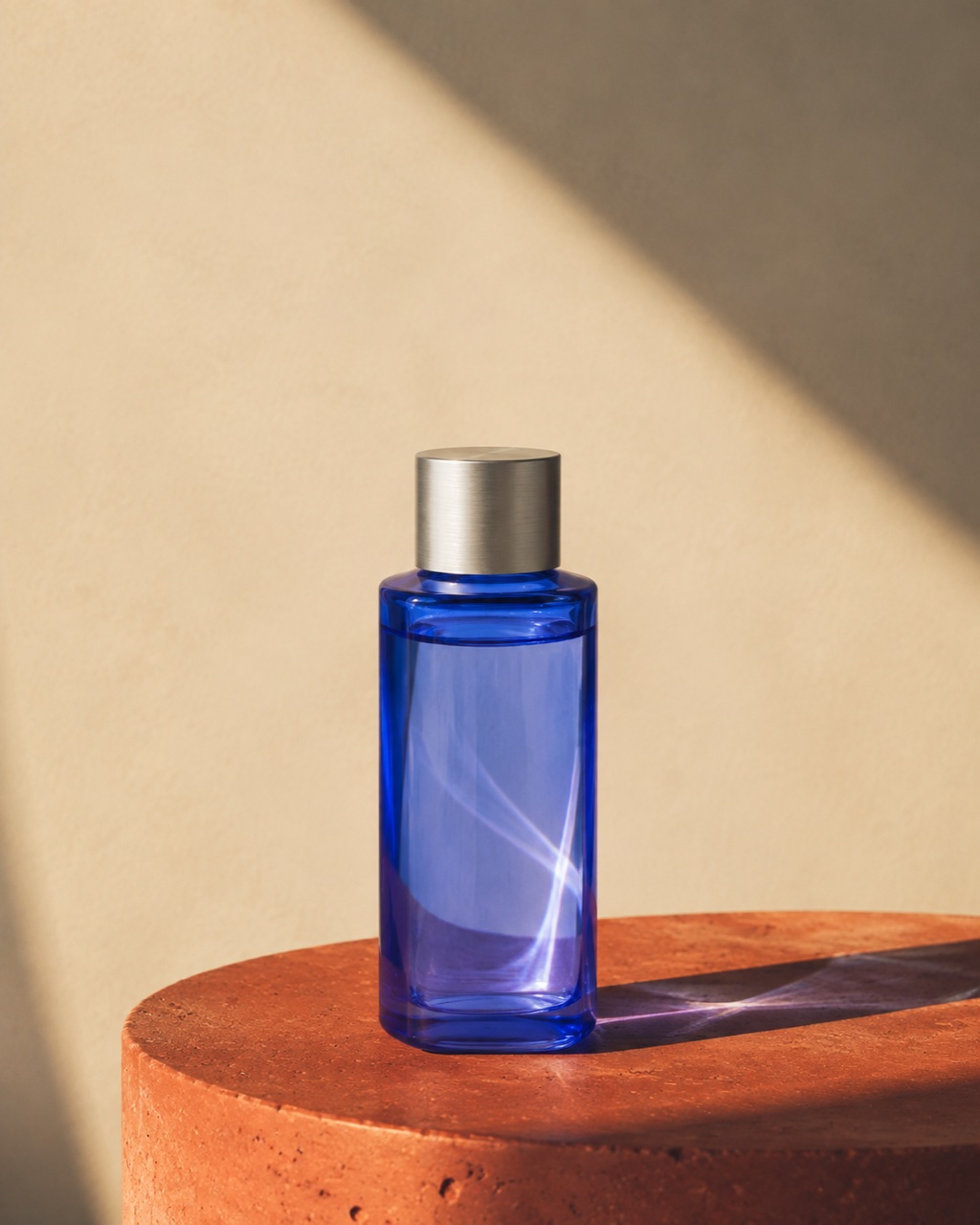 Cobalt glass skincare bottle in sunlight on a terracotta plinth